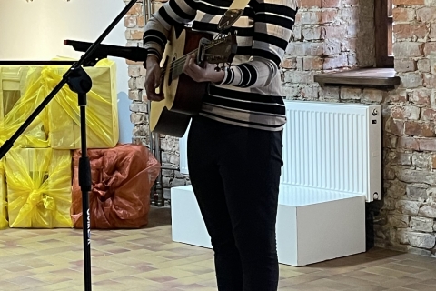 Moteris groja gitara ir dainuoja į mikrofoną. fone matyti meno kūriniai